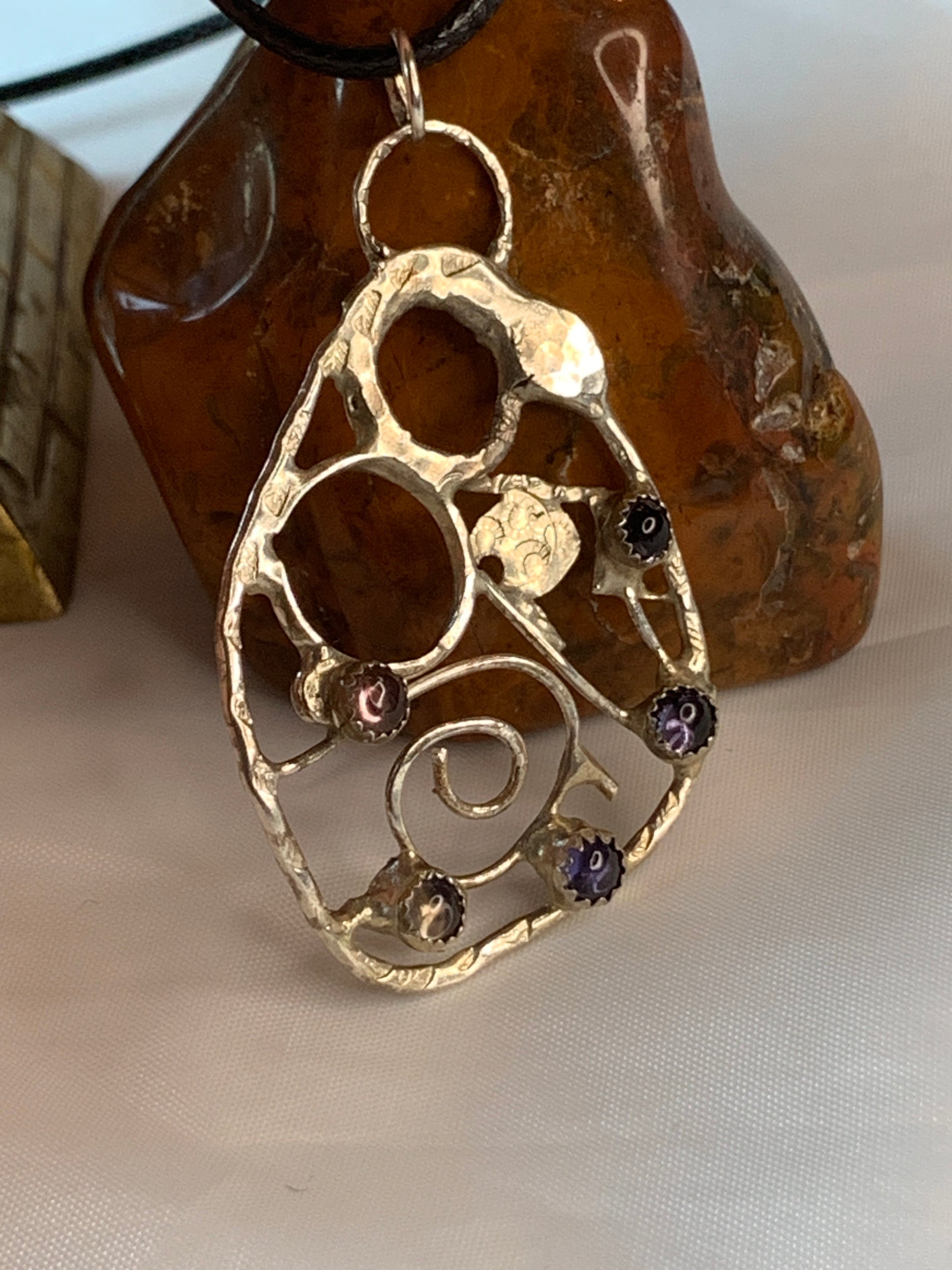 Nestled within this intricate framework are Tourmaline and Iolite gemstones, each radiating their unique energies. Tourmaline symbolizes creativity, protection, and balance, while Iolite represents inner vision and self-expression.