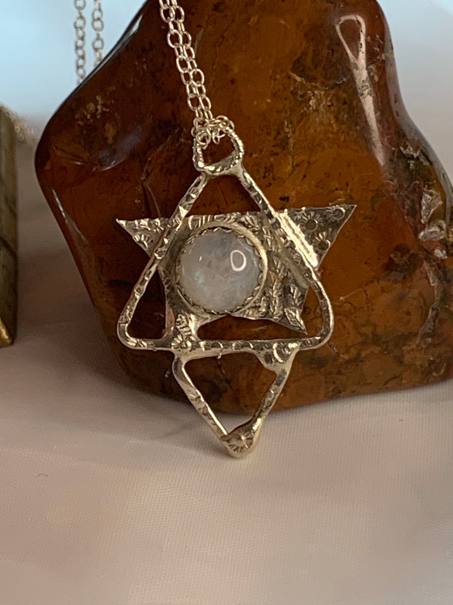 The pendant features a fusion of geometric shapes, creating a unique star pyramid or triangle design, all handcrafted from sterling silver. At its heart lies a luminous Moonstone gemstone, renowned for its enchanting play of colors and its connection to feminine energy and intuition.