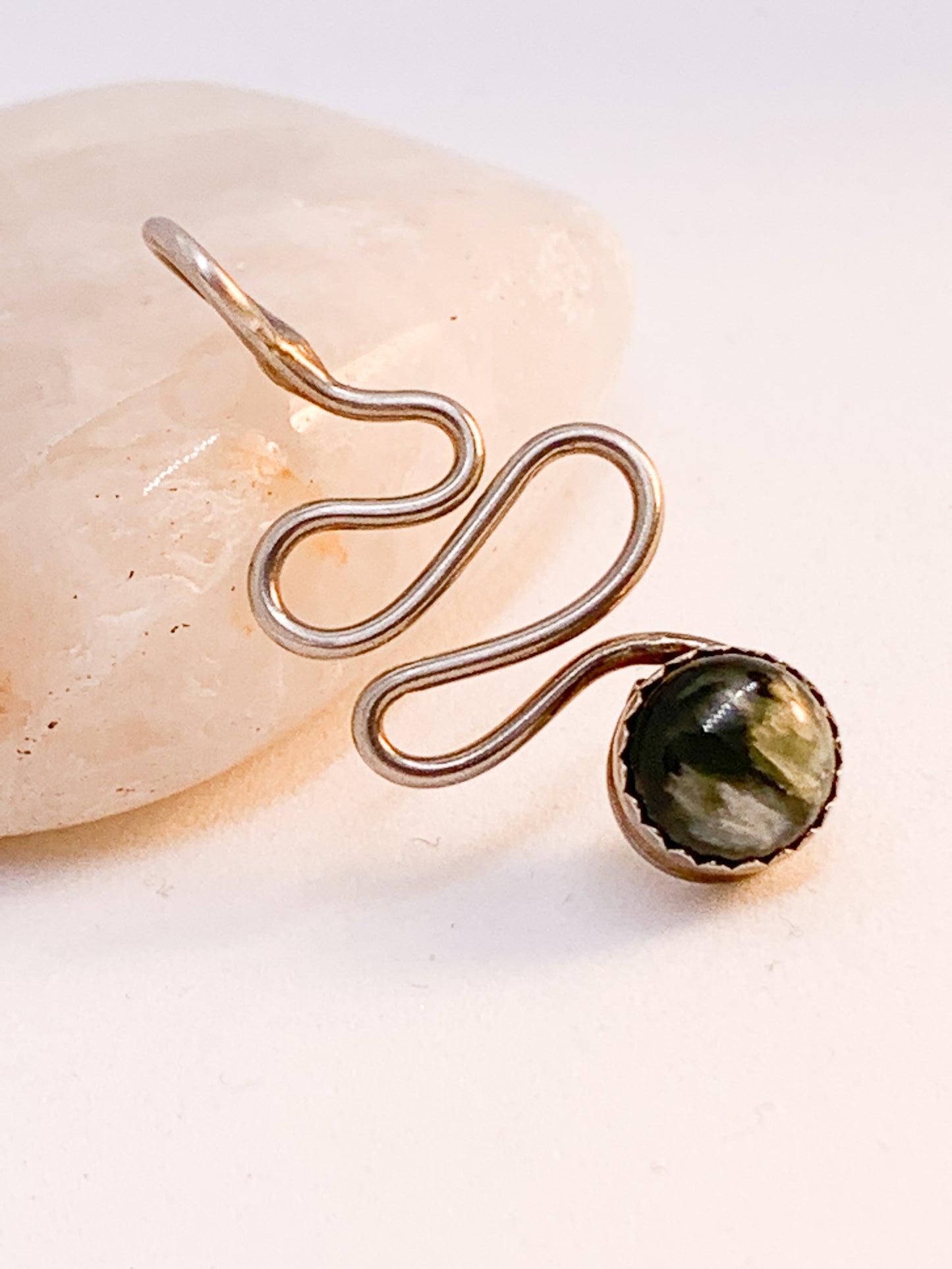 The pendant features a serene Seraphinite cabochon, hand-set in sterling silver, creating a stunning contrast between its silvery feather-like patterns and the deep, lush green hues of the stone.